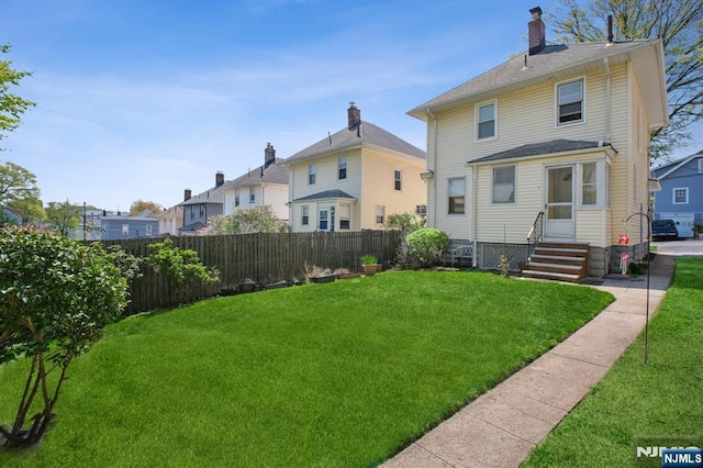 rear view of property featuring entry steps, a residential view, a chimney, fence, and a yard