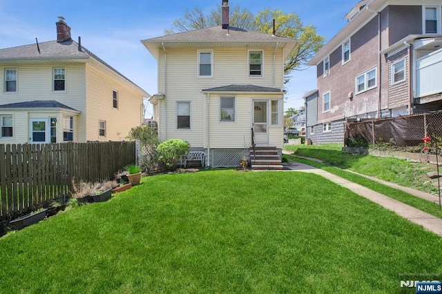rear view of house featuring a yard, entry steps, a chimney, and fence