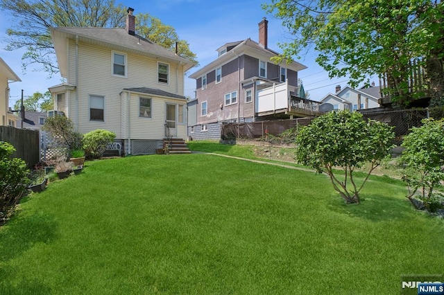 rear view of house featuring a lawn, entry steps, and fence