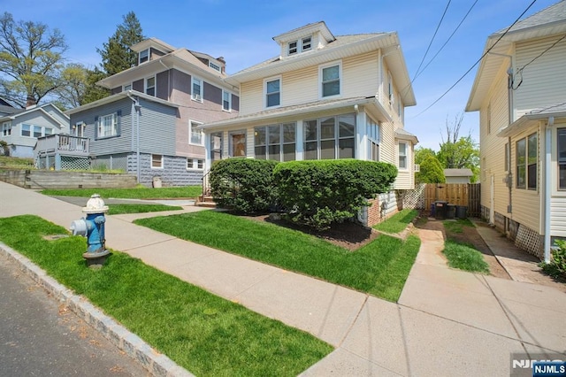 traditional style home with a sunroom, a front lawn, and fence