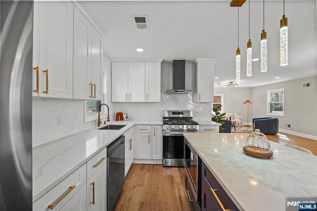 kitchen featuring recessed lighting, light wood finished floors, a sink, stainless steel appliances, and wall chimney exhaust hood
