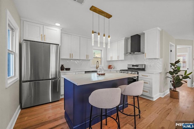 kitchen with light countertops, wall chimney range hood, stainless steel appliances, and decorative backsplash