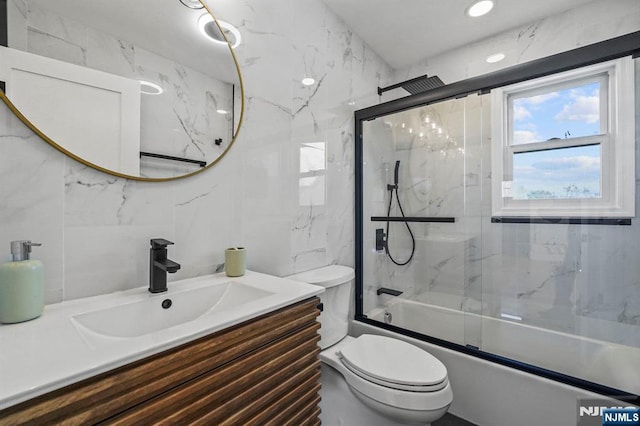 bathroom with tile walls, toilet, vanity, and enclosed tub / shower combo