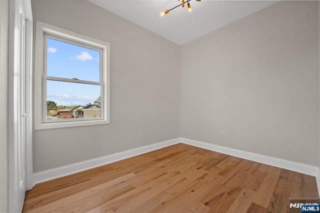 spare room featuring baseboards, wood finished floors, and an inviting chandelier