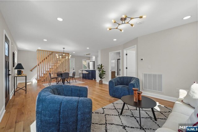 living area with an inviting chandelier, visible vents, light wood-style flooring, and stairs