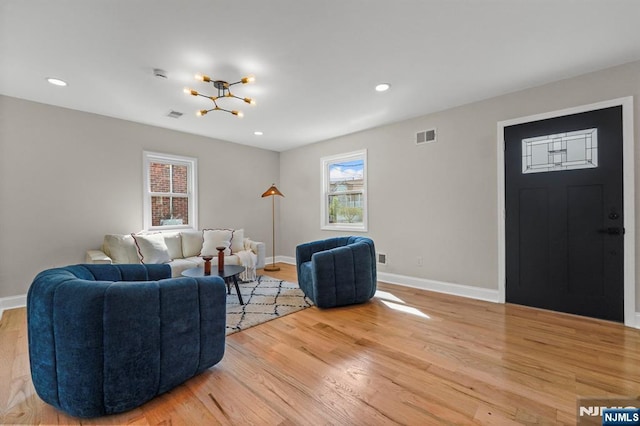 living room with light wood-type flooring, visible vents, a chandelier, and baseboards