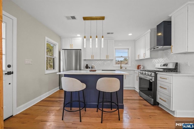 kitchen with stainless steel appliances, a kitchen bar, visible vents, white cabinetry, and wall chimney range hood