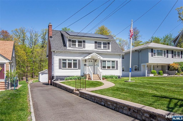 view of front of house featuring a detached garage, a front yard, a chimney, solar panels, and an outdoor structure
