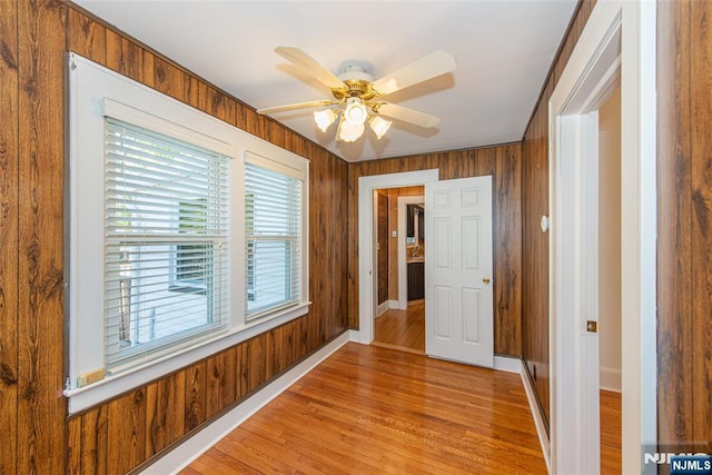spare room featuring wooden walls, baseboards, a ceiling fan, and light wood-style flooring