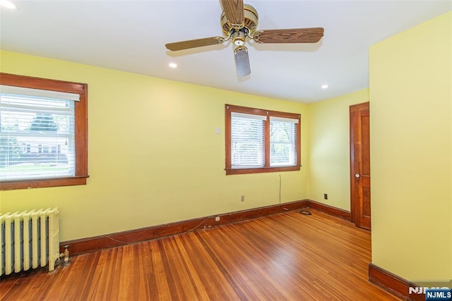 spare room with baseboards, radiator heating unit, a wealth of natural light, and wood finished floors
