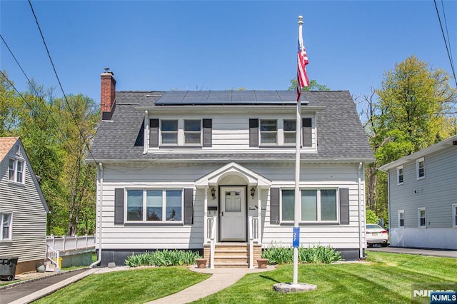 bungalow with roof mounted solar panels, a chimney, a shingled roof, and a front yard