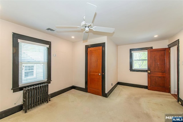 unfurnished bedroom featuring carpet flooring, ceiling fan, radiator, baseboards, and visible vents