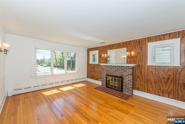unfurnished living room featuring wooden walls, baseboard heating, a fireplace, wood-type flooring, and baseboards