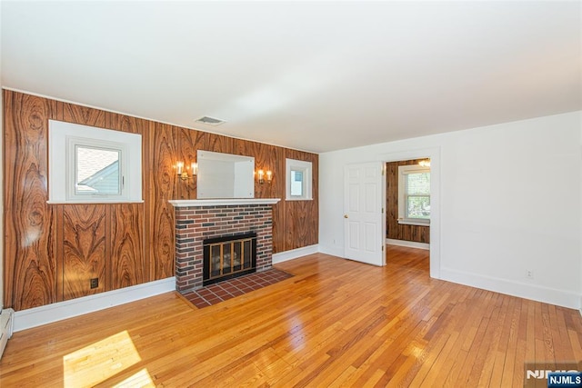 unfurnished living room with visible vents, a brick fireplace, wood walls, hardwood / wood-style flooring, and baseboards