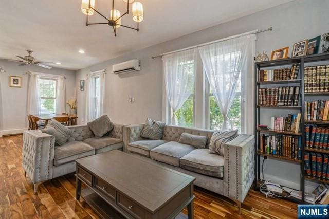 living area featuring a wall unit AC, wood finished floors, and ceiling fan with notable chandelier