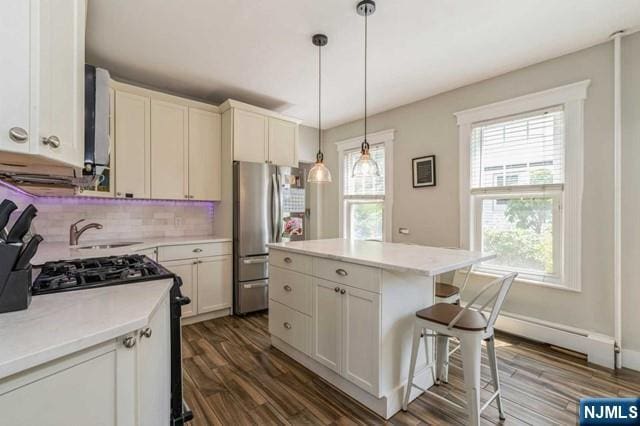kitchen featuring dark wood-style flooring, a sink, decorative backsplash, range with gas cooktop, and freestanding refrigerator