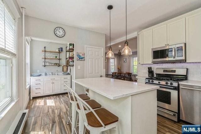 kitchen with stainless steel appliances, decorative backsplash, a breakfast bar, white cabinets, and wood finished floors