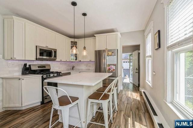 kitchen featuring stainless steel appliances, light countertops, a kitchen island, dark wood finished floors, and backsplash
