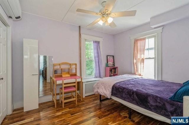 bedroom featuring radiator, ceiling fan, wood finished floors, and an AC wall unit