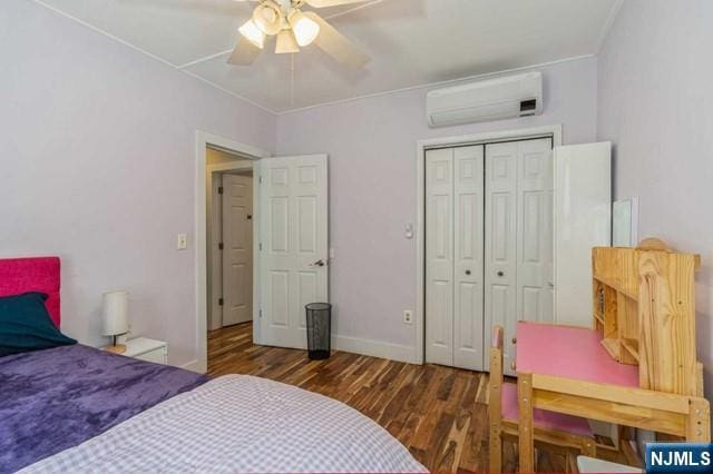 bedroom featuring wood finished floors, a closet, ceiling fan, an AC wall unit, and baseboards