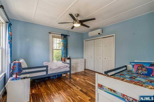 bedroom with wood-type flooring, an AC wall unit, a ceiling fan, and a closet