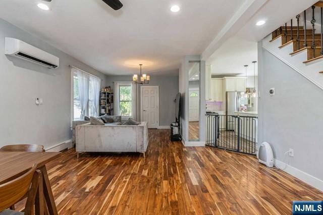 living room featuring stairway, baseboards, an inviting chandelier, wood finished floors, and a wall mounted air conditioner