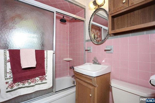 full bath with tile walls, shower / bath combination with glass door, toilet, and vanity