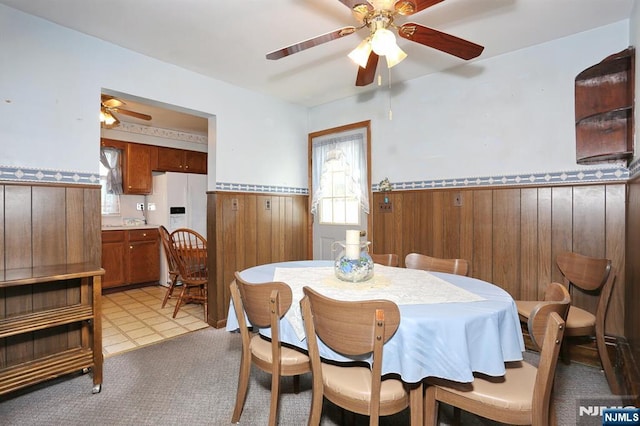dining area featuring wainscoting, light carpet, ceiling fan, and wooden walls