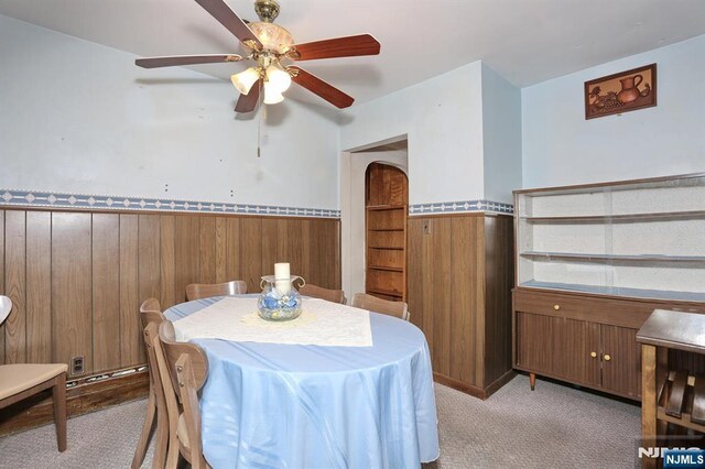carpeted dining room featuring wooden walls, a ceiling fan, and wainscoting