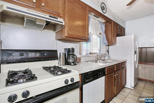 kitchen with a sink, brown cabinets, under cabinet range hood, white appliances, and light countertops