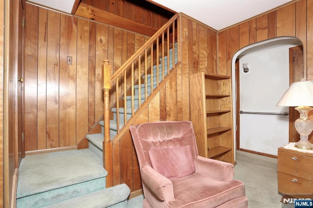 staircase featuring carpet, wooden walls, baseboards, and arched walkways
