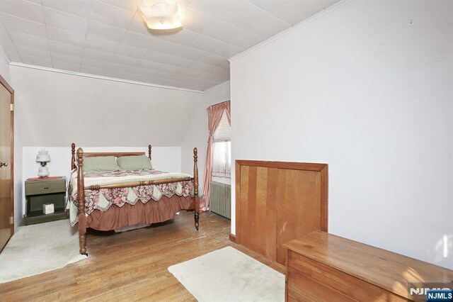 bedroom featuring crown molding, radiator heating unit, and wood finished floors