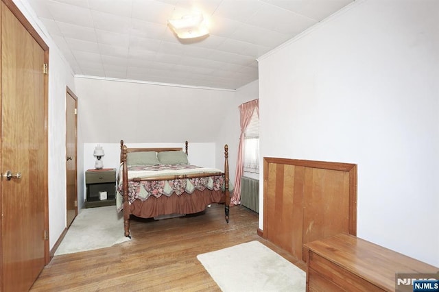 bedroom with radiator heating unit, wood finished floors, and crown molding