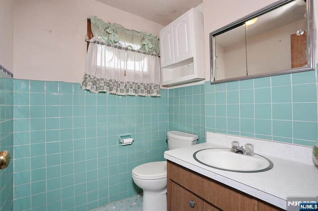 half bath featuring toilet, tile patterned floors, tile walls, and vanity