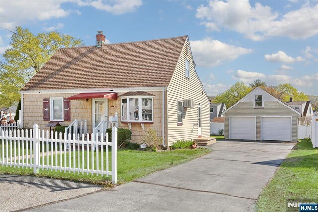 cape cod-style house with a detached garage, roof with shingles, a wall unit AC, a front lawn, and a fenced front yard