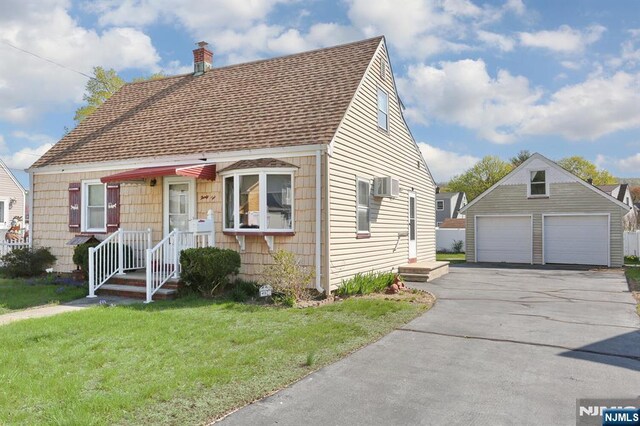 view of front of property with a chimney, a detached garage, roof with shingles, a wall mounted air conditioner, and a front yard