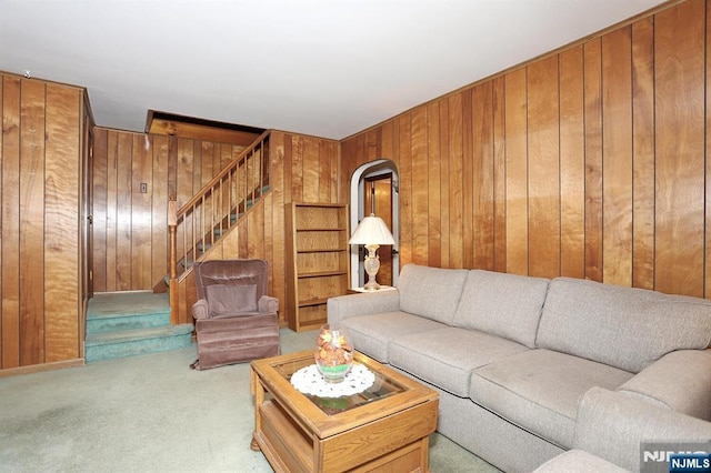 carpeted living room with wood walls, stairway, and arched walkways