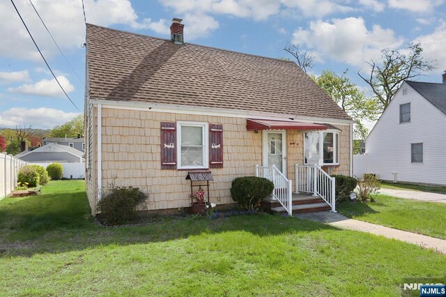 view of front of home with fence, a chimney, a shingled roof, and a front lawn