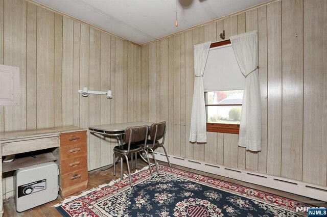 home office featuring wooden walls, a ceiling fan, baseboard heating, and wood finished floors