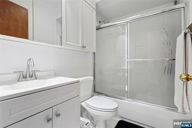 full bathroom with combined bath / shower with glass door, toilet, vanity, and decorative backsplash