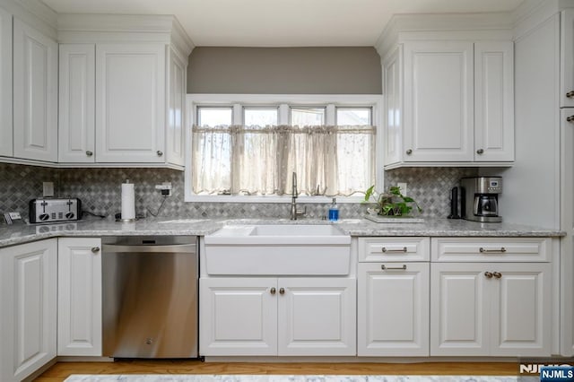 kitchen featuring tasteful backsplash, light stone countertops, dishwasher, a sink, and white cabinetry