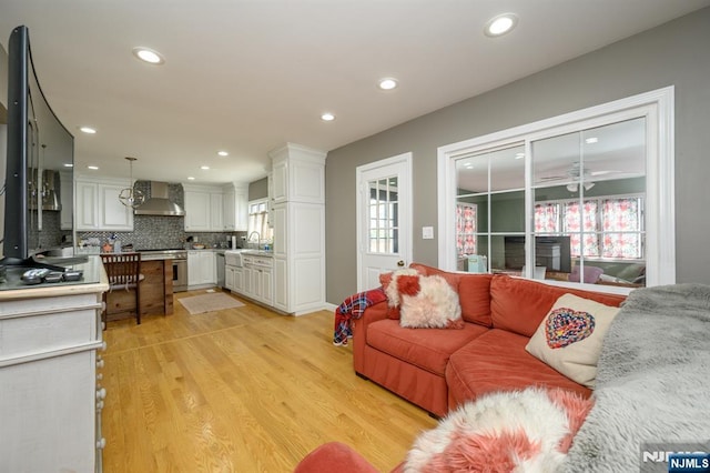 living room with light wood-type flooring, a ceiling fan, a healthy amount of sunlight, and recessed lighting