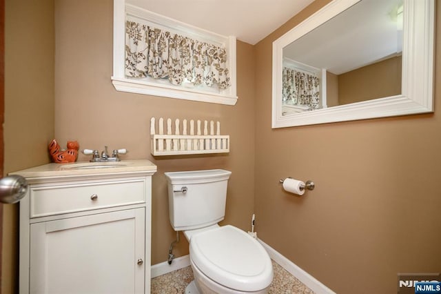 half bathroom featuring baseboards, toilet, and vanity