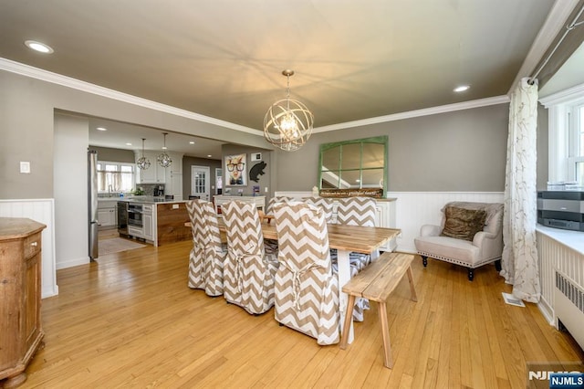dining area featuring light wood-style flooring, radiator heating unit, ornamental molding, a wainscoted wall, and a notable chandelier