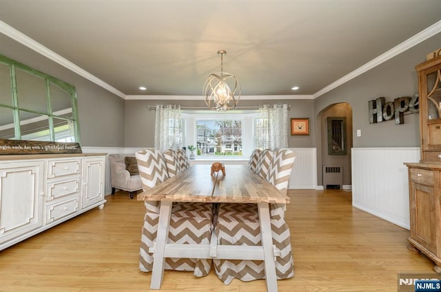 dining room with arched walkways, a chandelier, wainscoting, a wealth of natural light, and light wood-type flooring