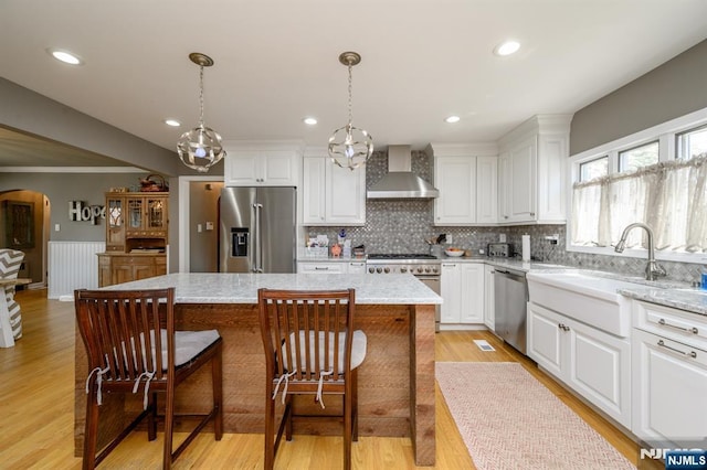 kitchen featuring wall chimney range hood, white cabinetry, arched walkways, a center island, and high quality appliances