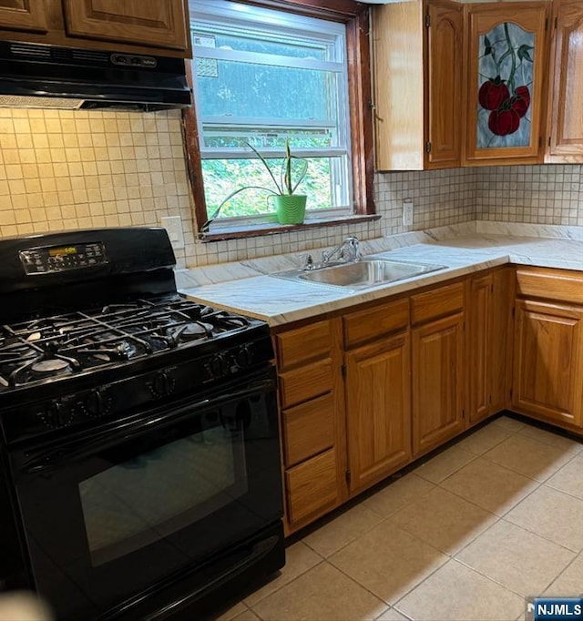 kitchen with tasteful backsplash, light tile patterned floors, under cabinet range hood, light countertops, and black gas range