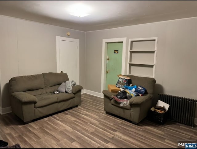 living area featuring radiator heating unit, wood finished floors, baseboards, and built in shelves