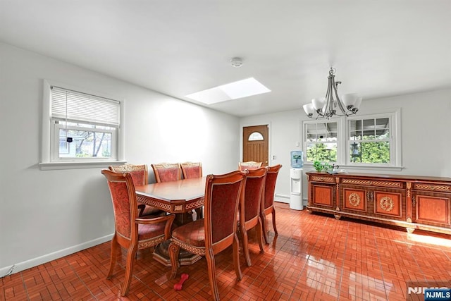 dining area featuring an inviting chandelier, a healthy amount of sunlight, brick patterned floor, and a skylight