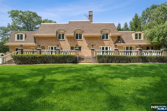 rear view of property featuring a yard, mansard roof, a chimney, and brick siding